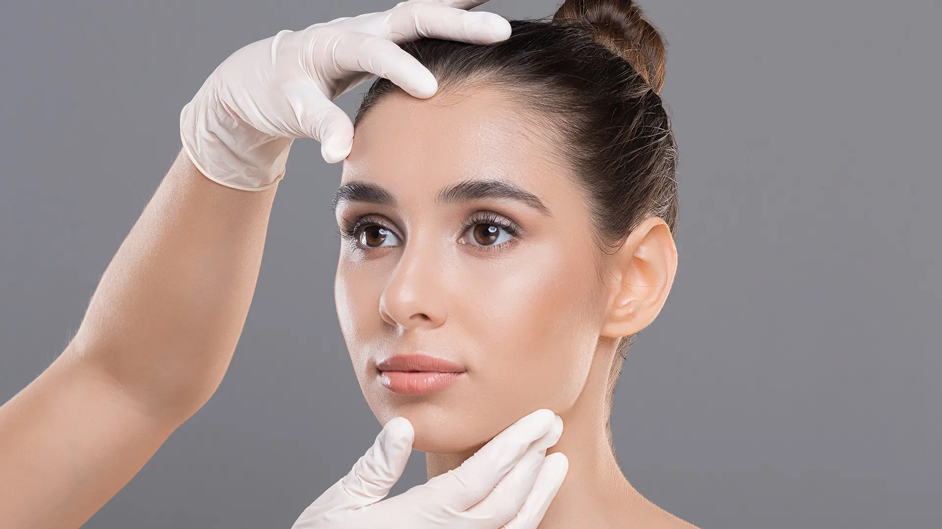 Cosmetologist examining young woman’s face before facial rejuvenation or cosmetic treatment at Dr. Sanaz Harirchian’s Houston facial plastic surgery clinic.